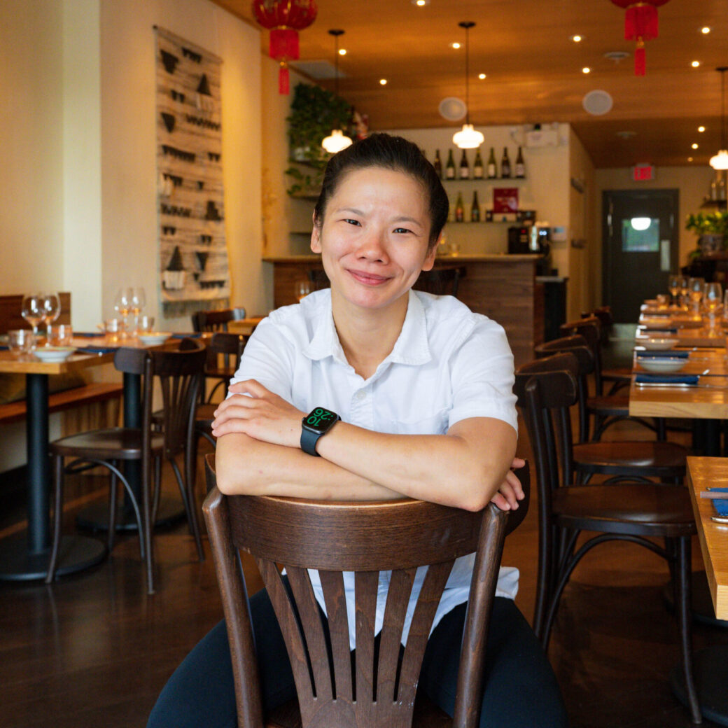 Woman with short black hair sitting backwards on a brown wooden chair in a restaurant. 