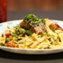 Seared salmon fillet topped with chopped herbs served over linguine pasta with a cream and vegetable sauce.