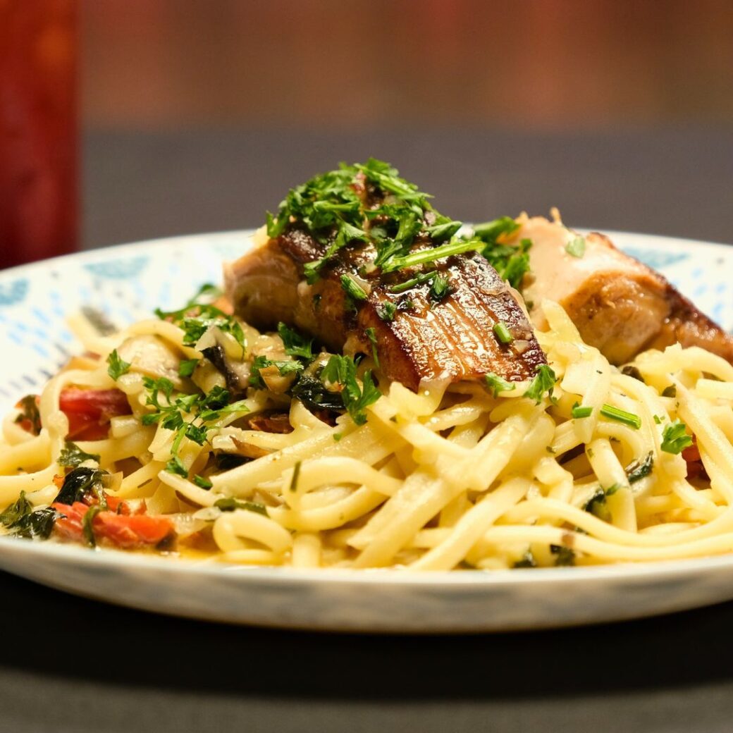 Seared salmon fillet topped with chopped herbs served over linguine pasta with a cream and vegetable sauce.