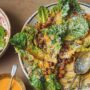 Romaine lettuce tossed with creamy orange dressing and crispy spiced chickpeas, topped with grated cheese, served on a plate with spoons and extra dressing on the side.