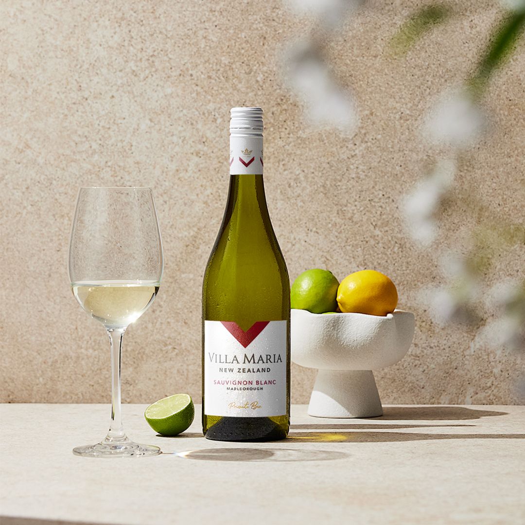 Bottle of Villa Maria Private Bin Sauvignon Blanc with wine glass and citrus fruit on a table.