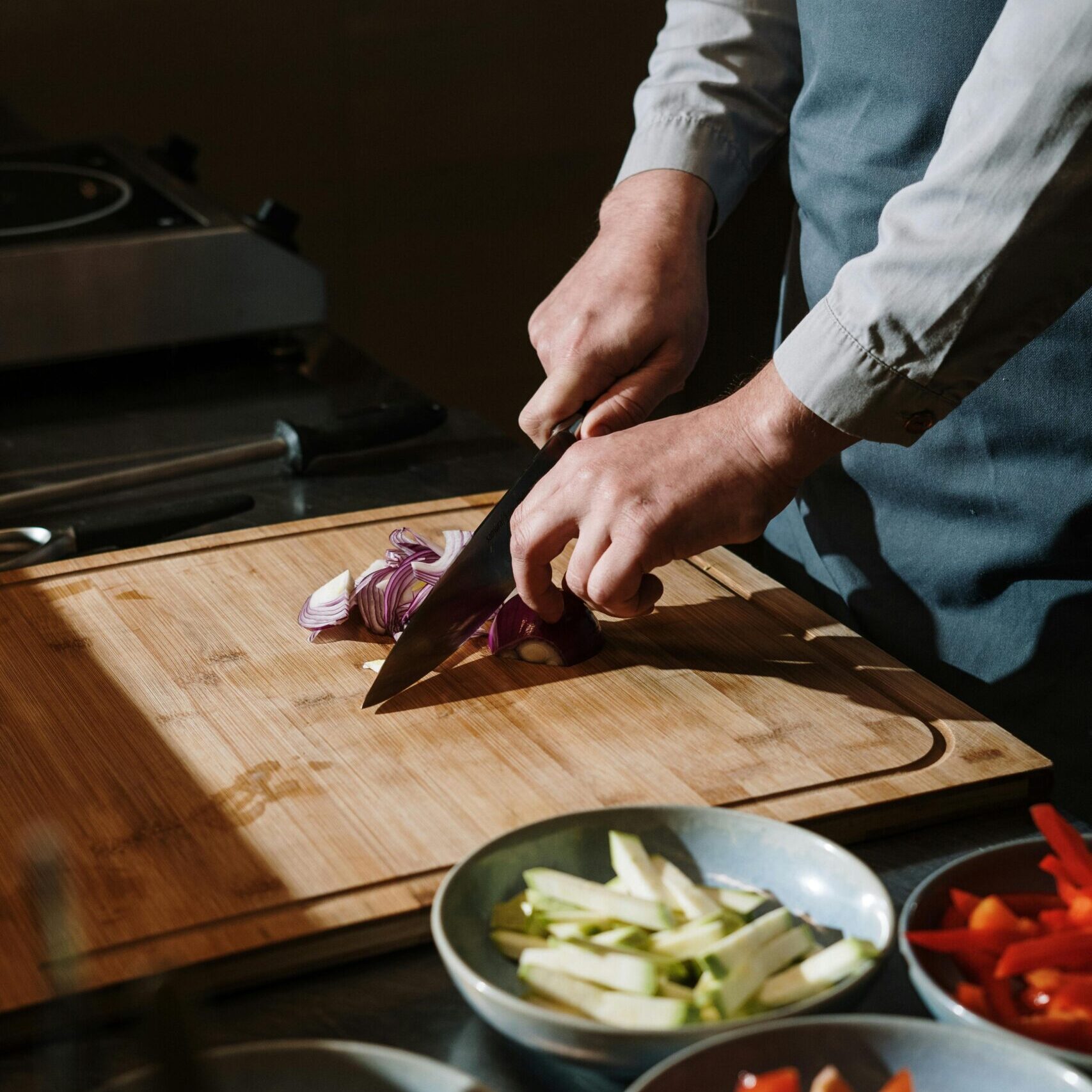 Close-up of hands using a chef's knife to chop a red onion on a wooden cutting board.