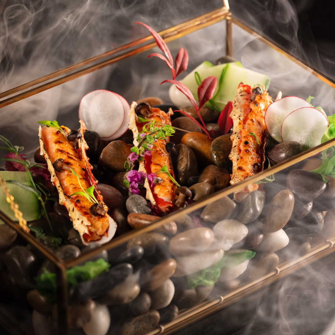 Three grilled Alaskan king crab legs in a decorative clear box.