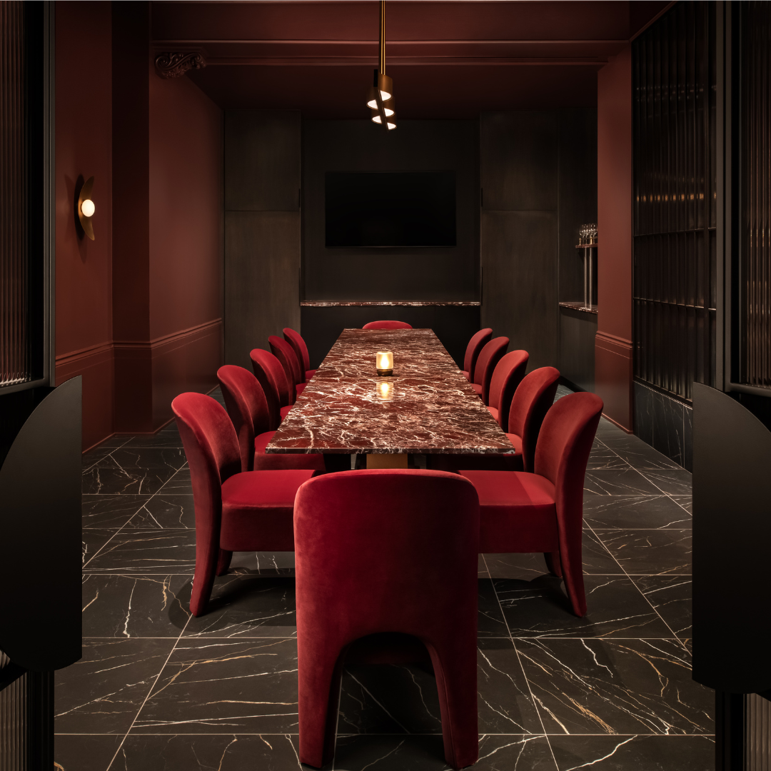 A private dining room with red velvet chairs and a long red marble table.