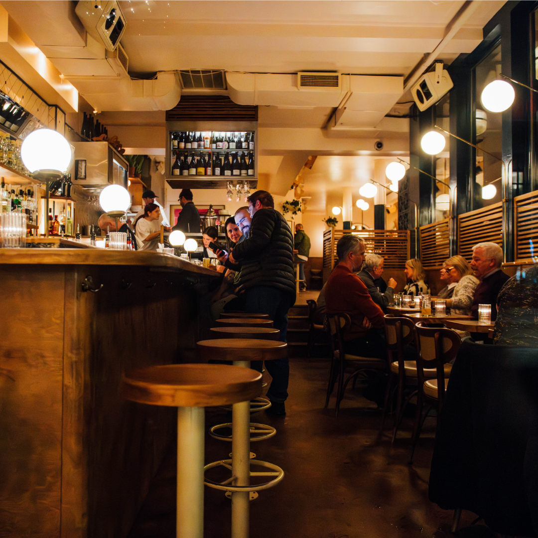 A warmly lit bar with people sitting on barstools and in booths.