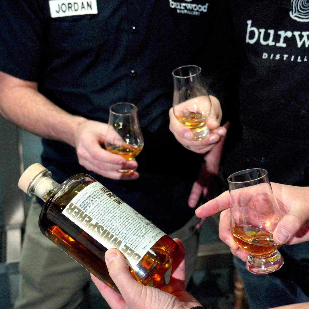 Close-up of three people holding whisky glasses and a bottle of whisky. 
