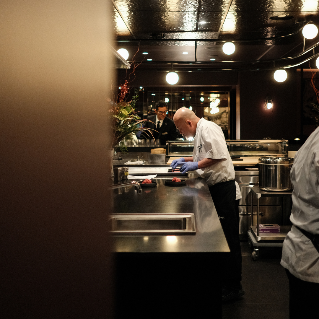 A man in a white chef's coat using tweezers to place thinly sliced tuna on a plate. 