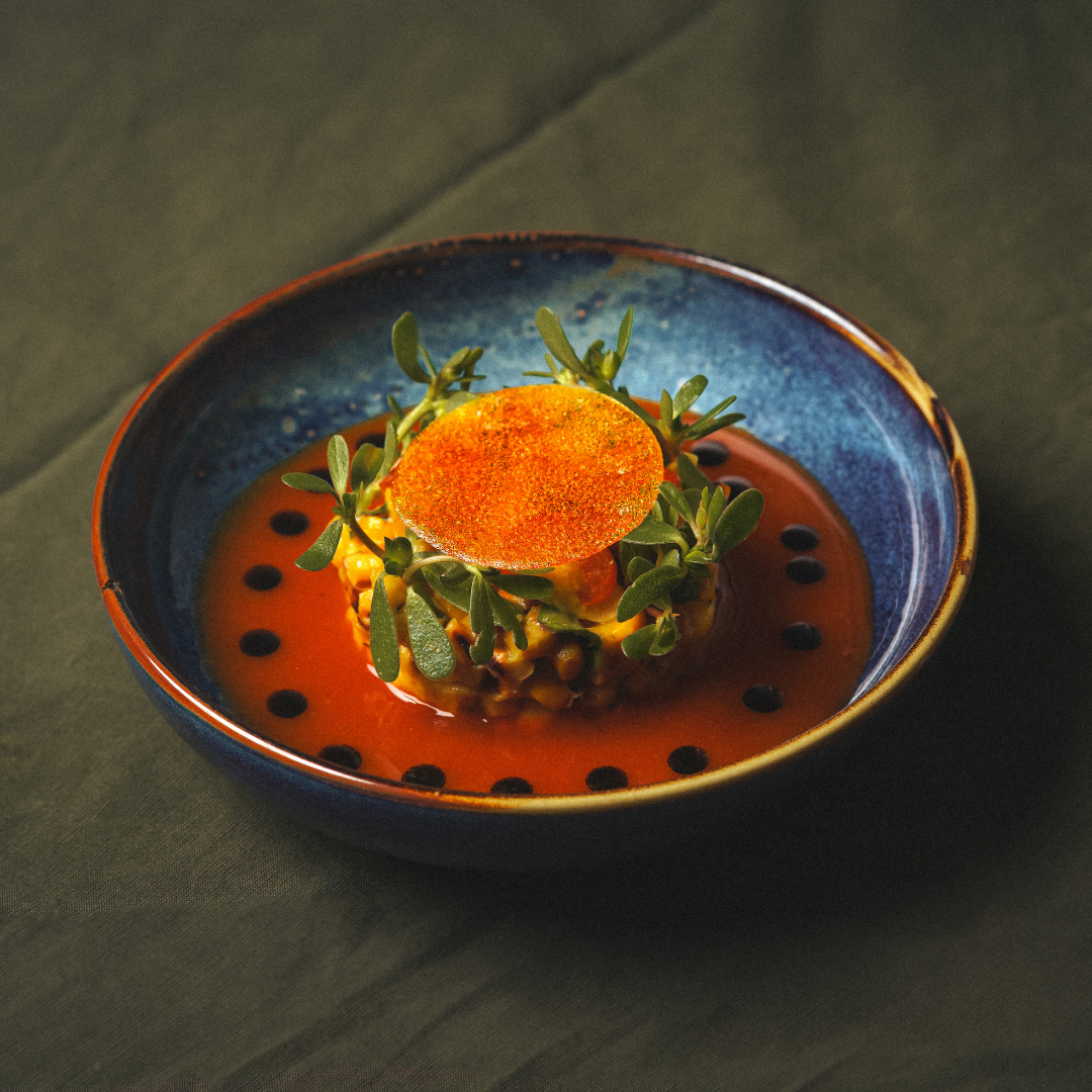 Corn risotto in a red sauce topped with arugula in a blue plate.