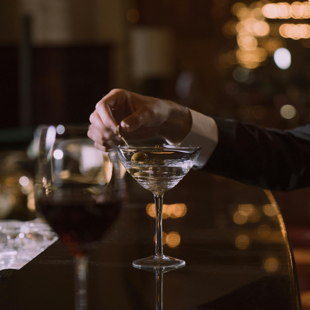 Close-up of a hand holding the olive skewer of a dry martini at the bar. 