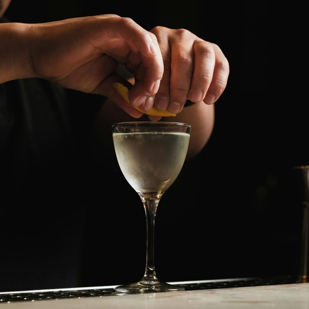 Close-up of hands zesting a lemon twist over an ice cold dry martini.