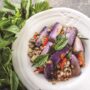 Eggplant stir-fry with Thai basil, ground meat and red chilies, served on a white plate with fresh basil nearby.