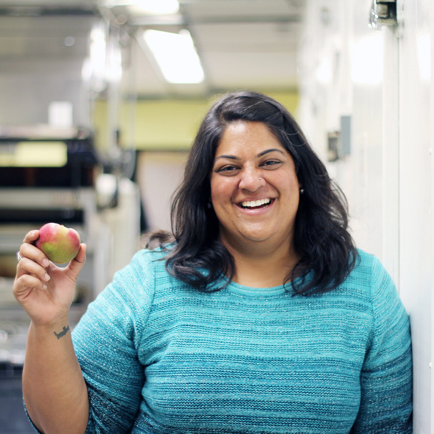 Woman in blue striped shirt smiling and holding an apple.