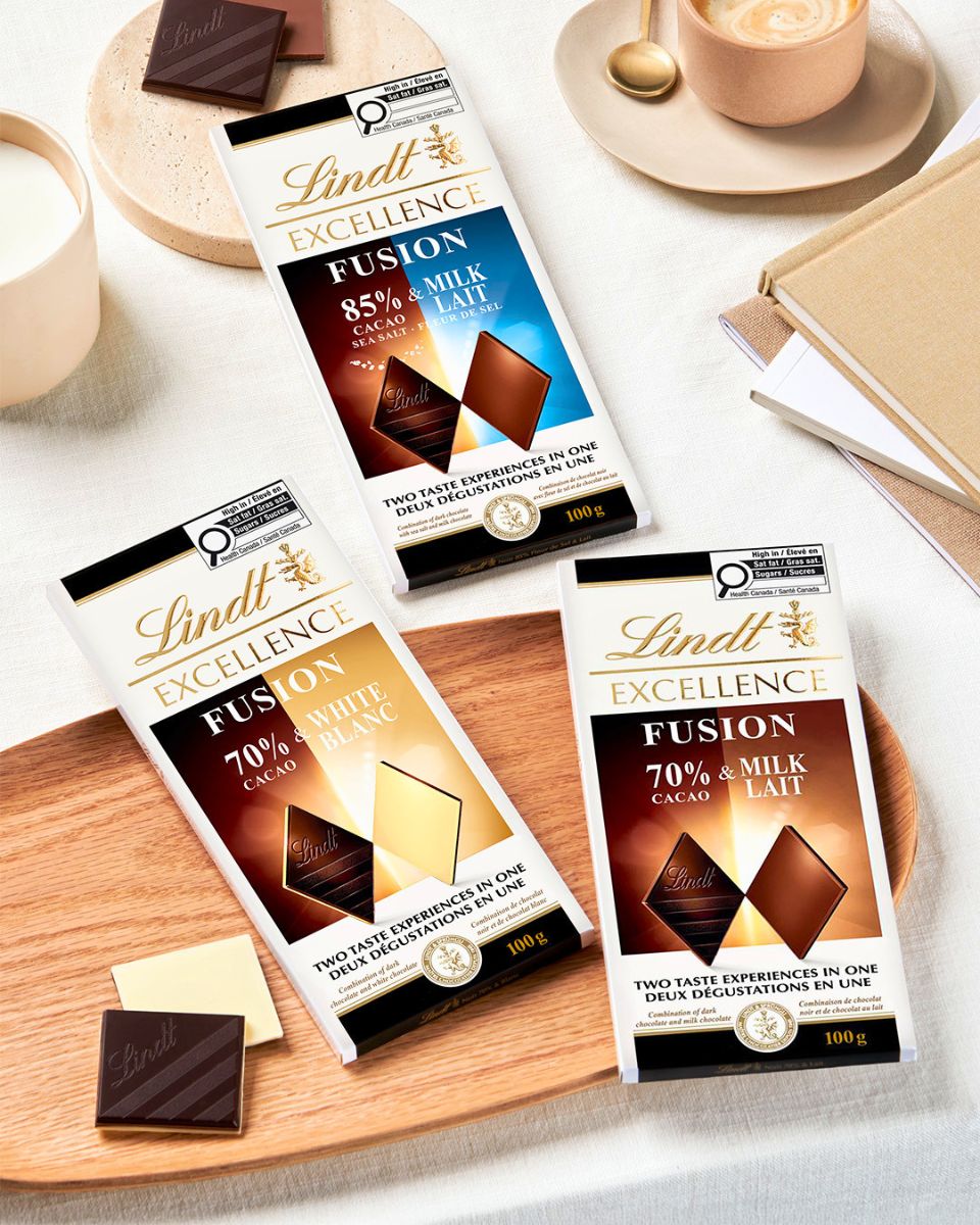 Lindt Excellence Fusion chocolate bars in three flavours—70% cacao with milk, 70% cacao with white, and 85% cacao sea salt and milk—arranged on a table with coffee and chocolate pieces