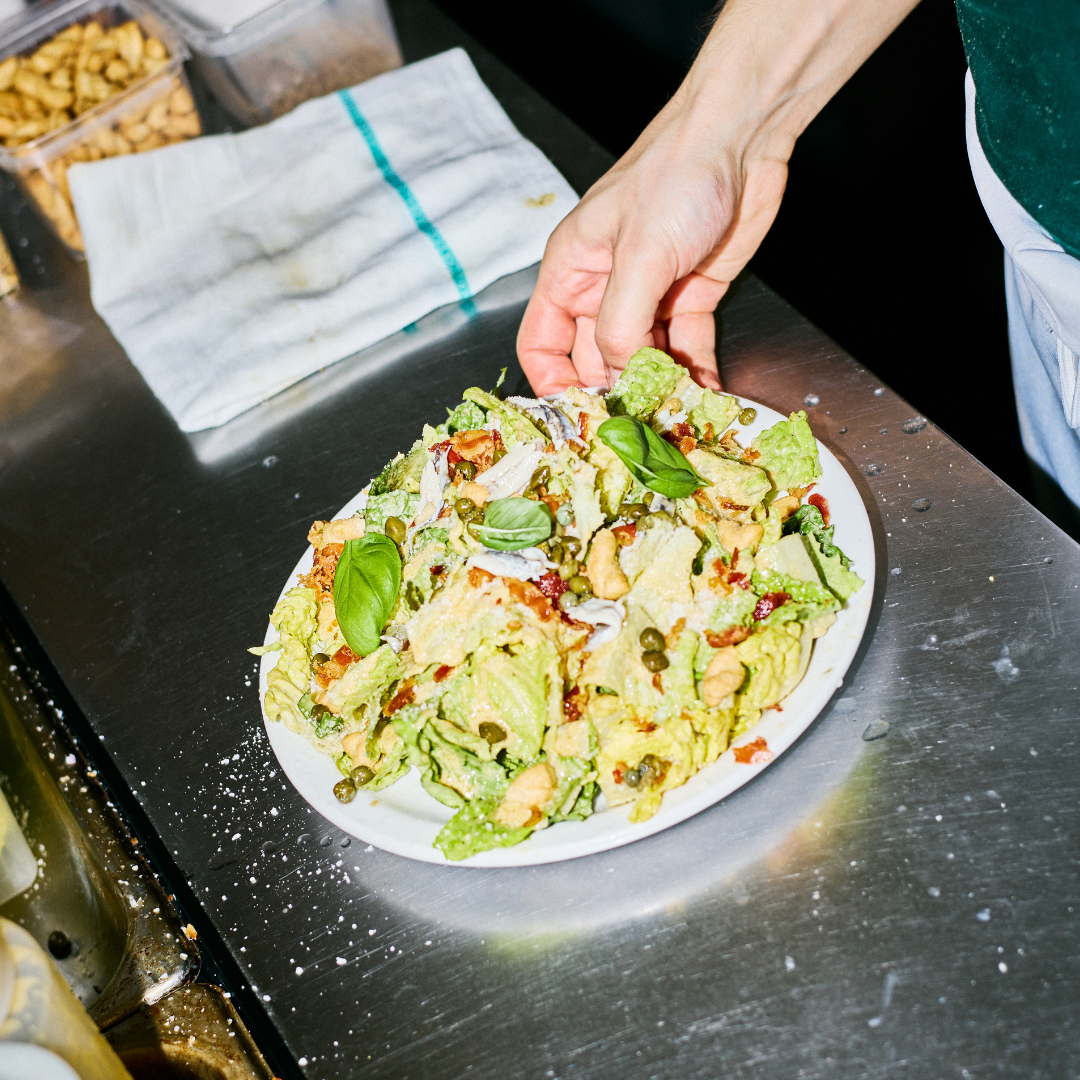 Hand placing a bowl of Caesar salad on a counter.