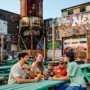 Four people drinking beer while sitting outside at a green bench.