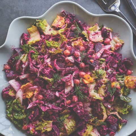 Beet salad with lettuce, chickpeas and fresh herbs in a white serving bowl, dressed in a vibrant pink vinaigrette.