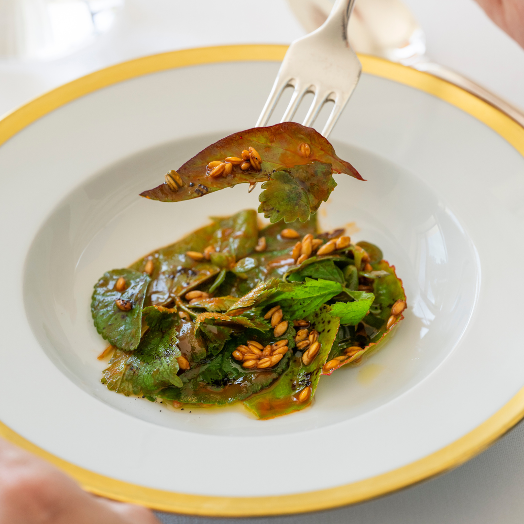 Close-up of a silver fork picking up a bite of wild greens with spelt from a white plate. 