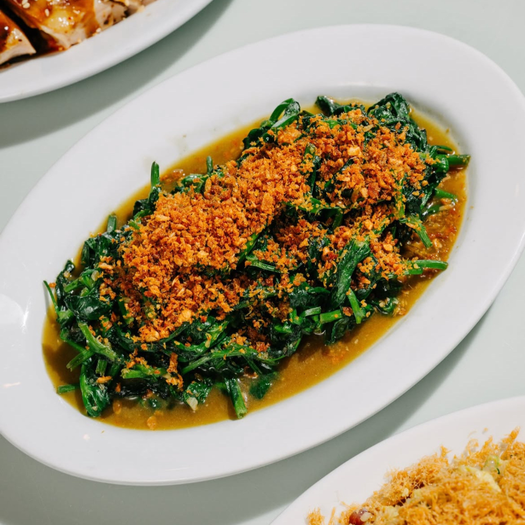 Stir fried snow pea leaves topped with crispy garlic on a white plate.