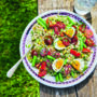 Italian-style rice bowl with asparagus, cherry tomatoes and soft-boiled eggs, served outdoors on a rustic wooden table with a glass of water.