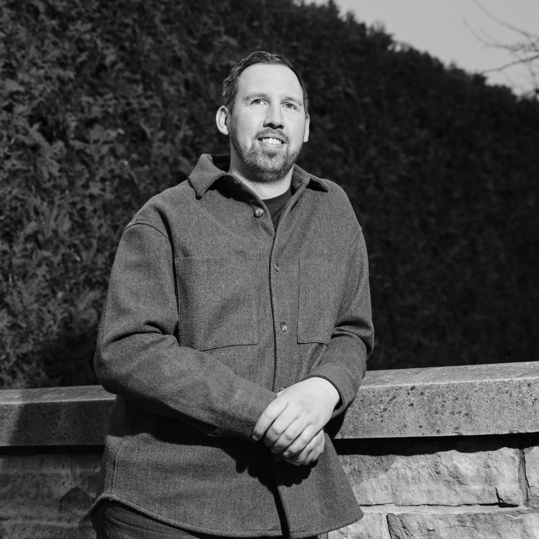 Black and white image of a smiling man leaning against a stone ledge.