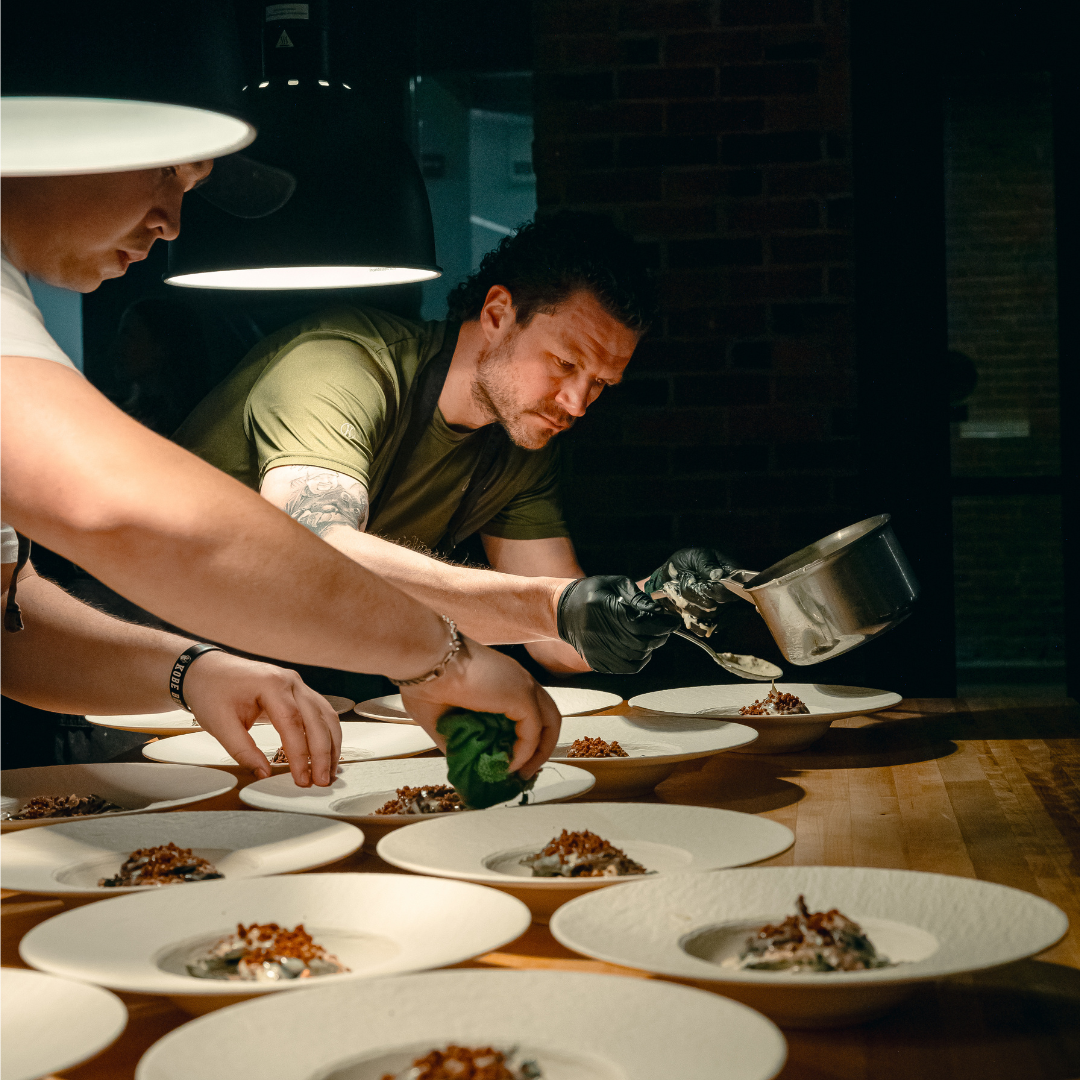 Two men plating thirteen plates on a wooden table. 