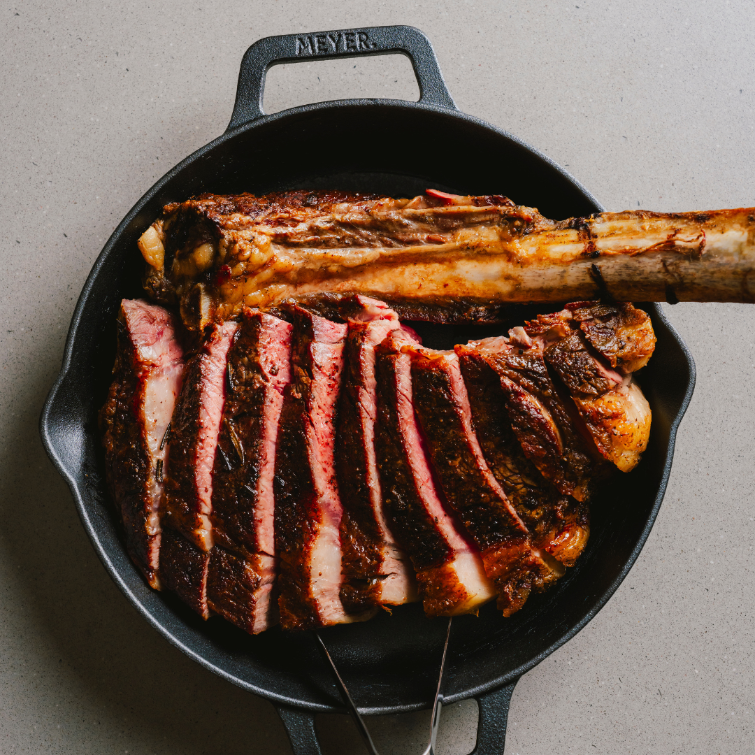 Sliced bone-in tomahawk steak in a cast-iron pan.