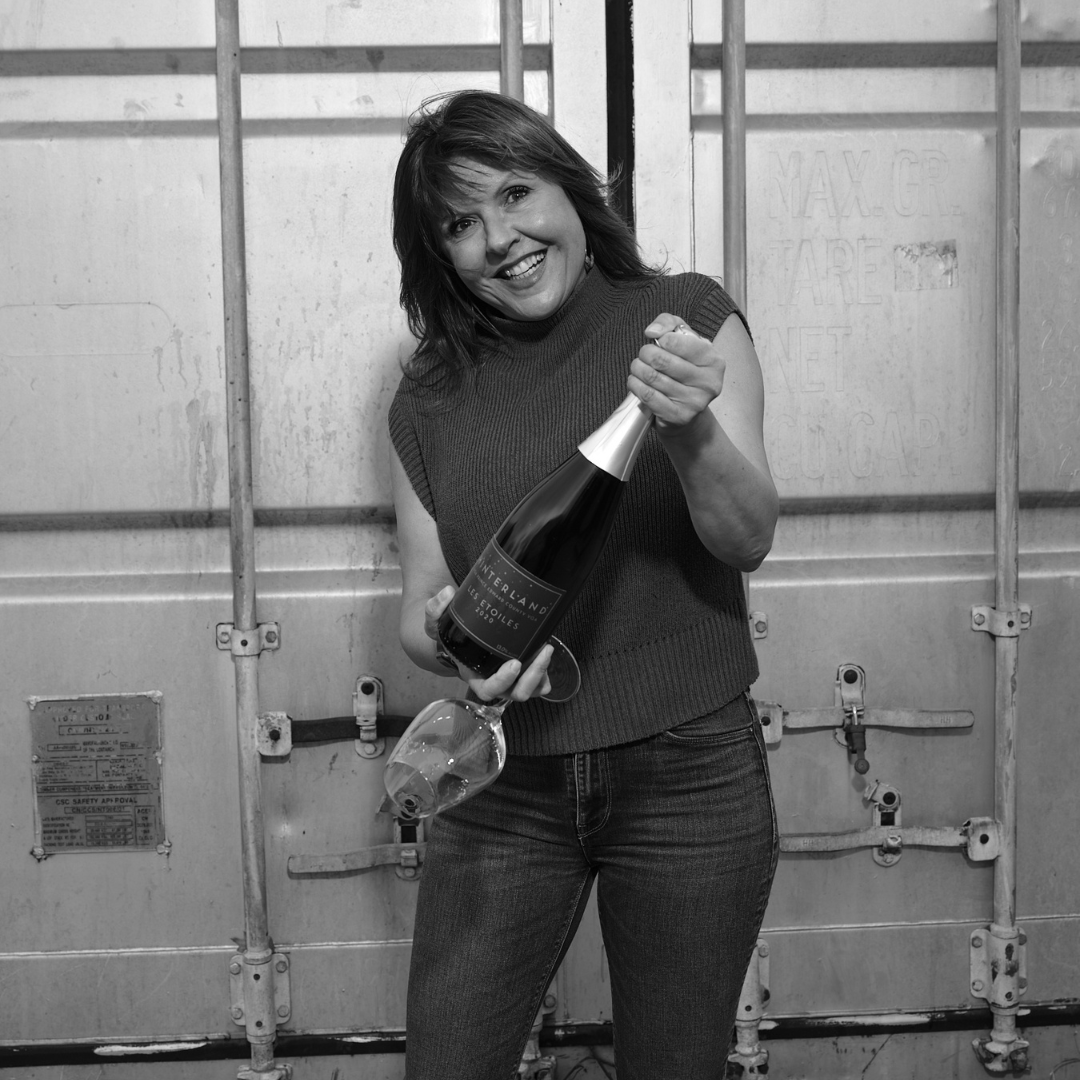 Black and white image of a smiling woman holding a bottle of wine. 
