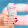 Hand holding a white a ready-to-drink RTD canned cocktail with a pool floatie in the water in the background.