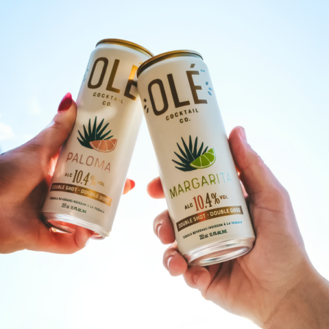Two hands cheersing white canned cocktails.