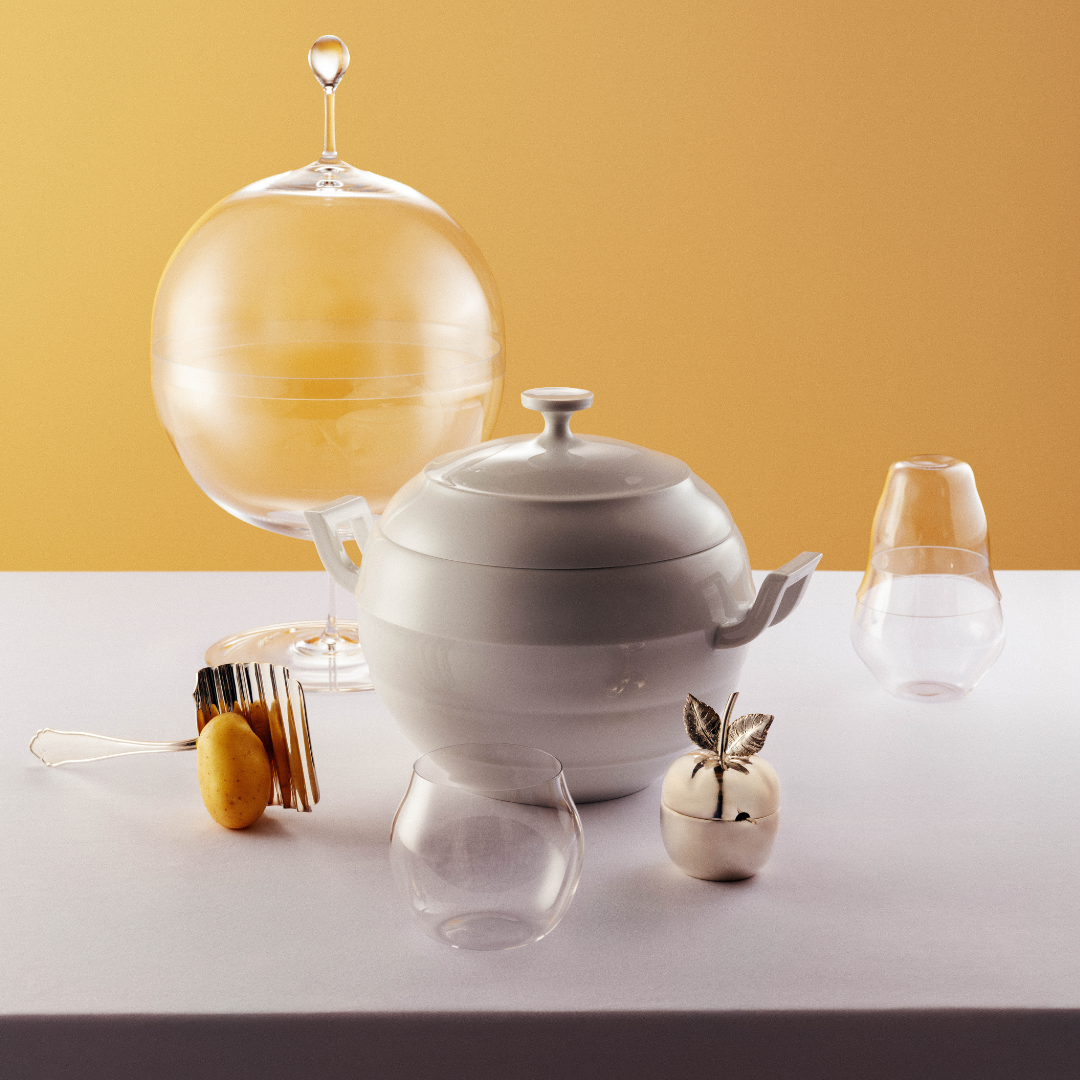 A tablescape featuring glassware and a white teapot on a white table with yellow backdrop. 