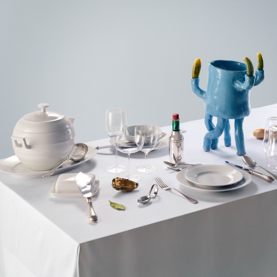 A tablescape on a table with a white tablecloth, including a ceramic vase, white plates, teapot and silverware.