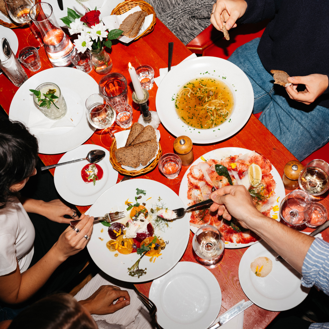 Overhead shot of people eating from communal plates on a red table.